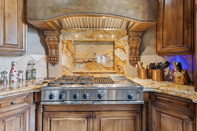 kitchen featuring light stone counters, decorative backsplash, custom exhaust hood, and stainless steel gas stovetop