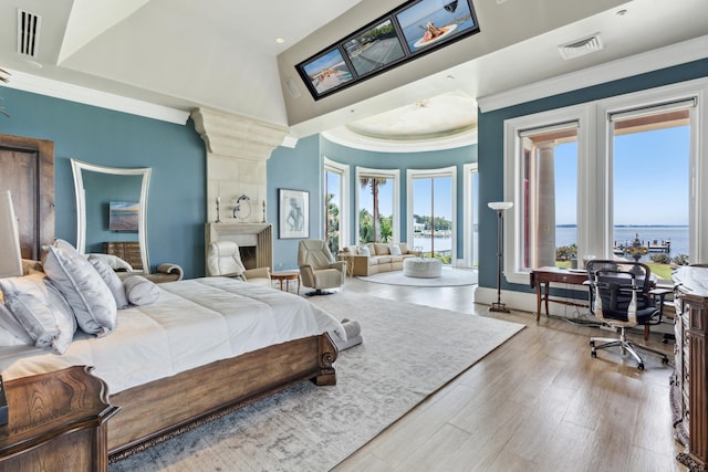 bedroom with a fireplace, light hardwood / wood-style flooring, a water view, and a towering ceiling