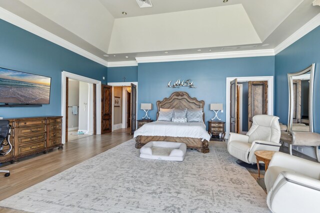 bedroom with a tray ceiling, a high ceiling, wood finished floors, a walk in closet, and ornamental molding