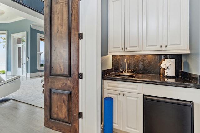 kitchen with decorative backsplash, white cabinetry, ornamental molding, sink, and light wood-type flooring