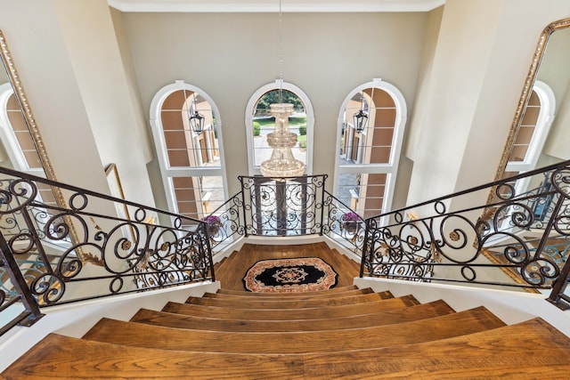 stairway featuring a towering ceiling, ornamental molding, and wood-type flooring