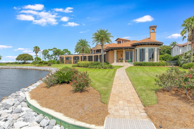 back of house with stucco siding, a water view, a tiled roof, and a yard