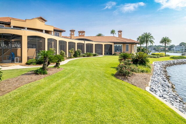 back of property featuring stucco siding, a water view, a sunroom, and a yard