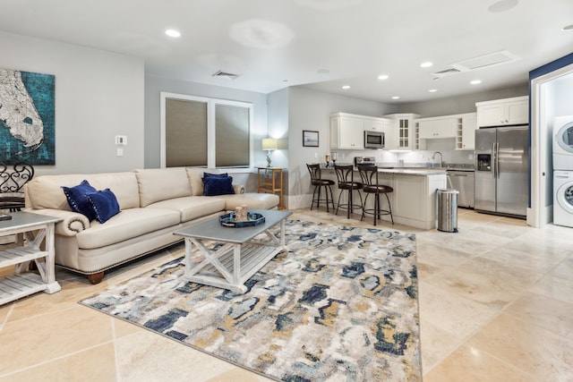 living room featuring light tile patterned floors, stacked washer / dryer, and sink