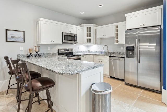 kitchen featuring white cabinets, a peninsula, appliances with stainless steel finishes, a sink, and light stone counters