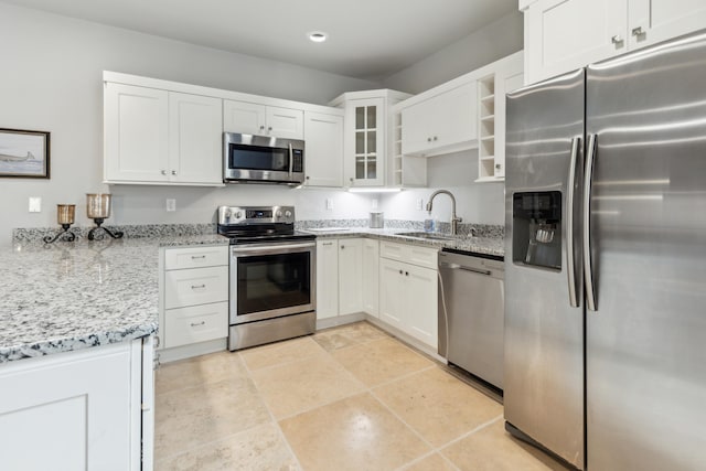 kitchen featuring light stone countertops, stainless steel appliances, glass insert cabinets, white cabinetry, and a sink