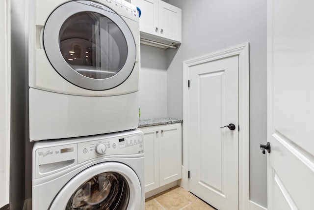 clothes washing area featuring light tile patterned floors, stacked washer and dryer, and cabinets