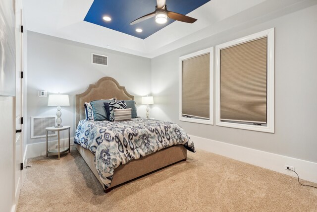 carpeted bedroom with ceiling fan and a tray ceiling