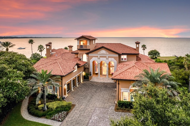 mediterranean / spanish home with stucco siding, an attached garage, a balcony, decorative driveway, and a water view