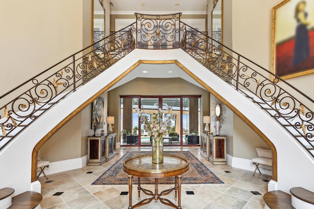 foyer entrance featuring a towering ceiling, baseboards, stairway, and crown molding