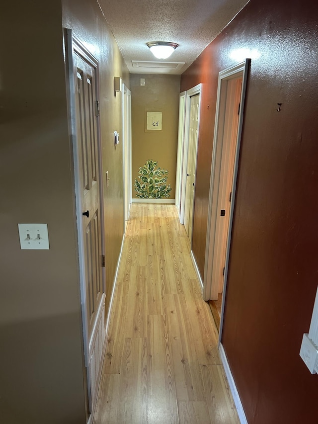 corridor with light wood-type flooring and a textured ceiling