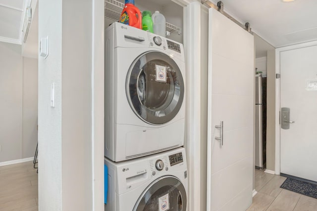 laundry area with a barn door, light wood-style flooring, laundry area, baseboards, and stacked washer and clothes dryer