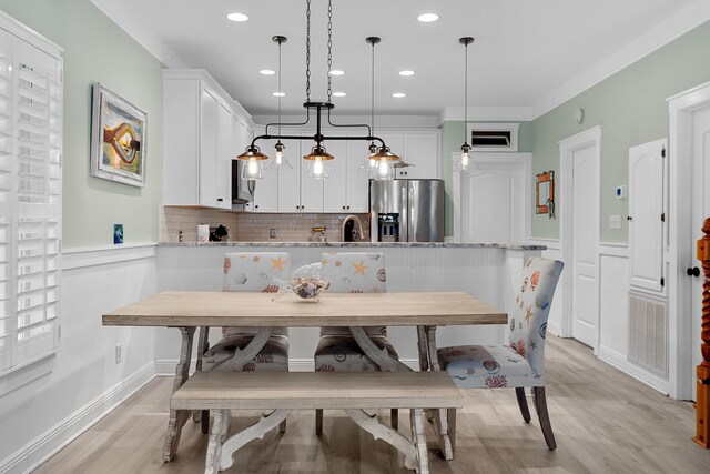 kitchen with crown molding, hanging light fixtures, backsplash, white cabinetry, and stainless steel fridge