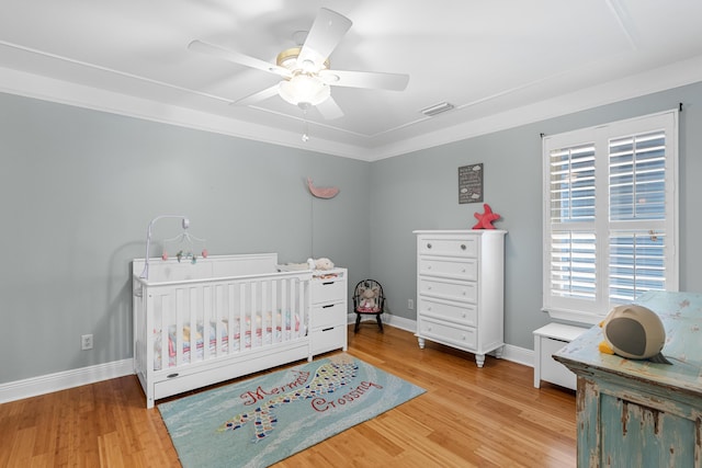 bedroom featuring wood-type flooring, a nursery area, and ceiling fan