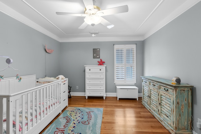 bedroom featuring a crib, light hardwood / wood-style flooring, ornamental molding, and ceiling fan