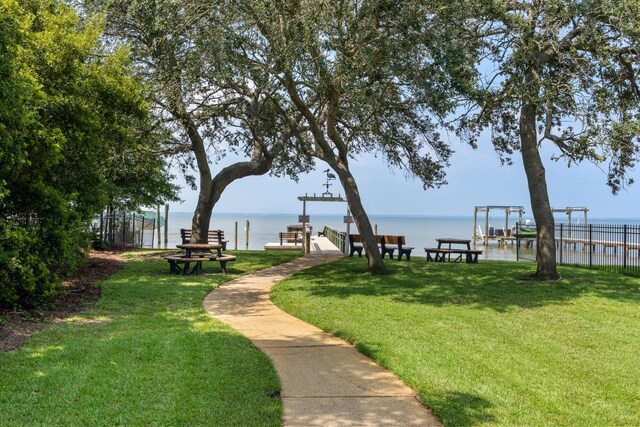 surrounding community with a boat dock, a water view, and a yard