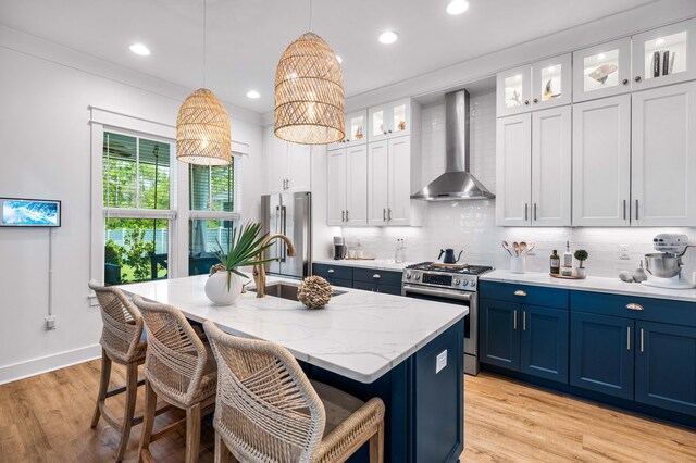 kitchen with hanging light fixtures, white cabinetry, premium appliances, a center island with sink, and wall chimney range hood