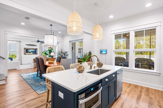 kitchen with decorative light fixtures, a kitchen island with sink, sink, and light hardwood / wood-style flooring