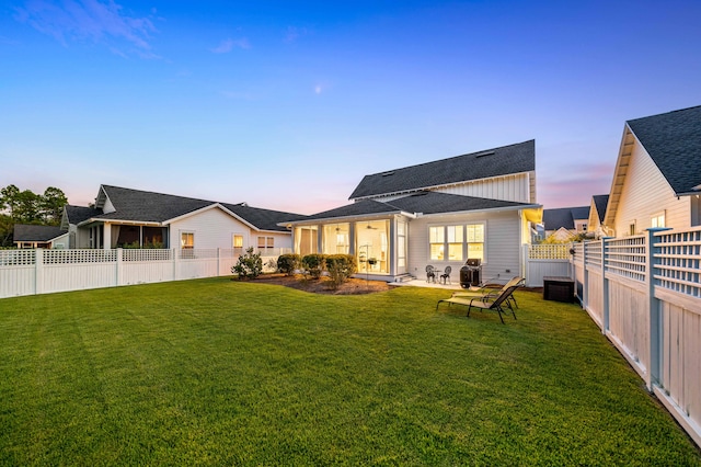 back house at dusk with a lawn and a patio area