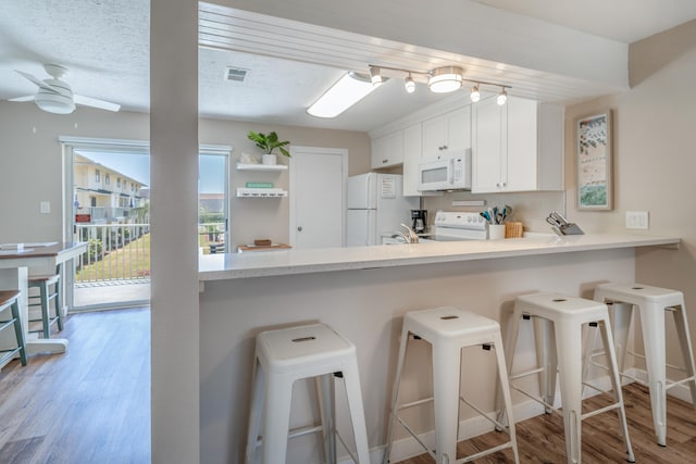 kitchen with light hardwood / wood-style floors, ceiling fan, a breakfast bar, white cabinetry, and white appliances