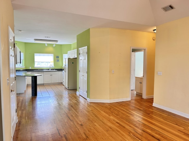 kitchen with white cabinetry, sink, light wood-type flooring, and white refrigerator