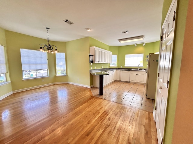 kitchen with sink, white cabinetry, hanging light fixtures, light hardwood / wood-style flooring, and white appliances