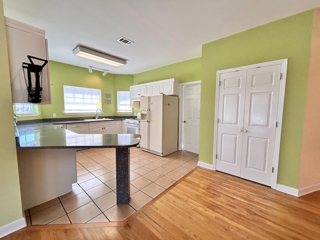 kitchen with sink, white cabinetry, light hardwood / wood-style flooring, kitchen peninsula, and white appliances