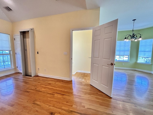 unfurnished room with an inviting chandelier, lofted ceiling, and light hardwood / wood-style flooring