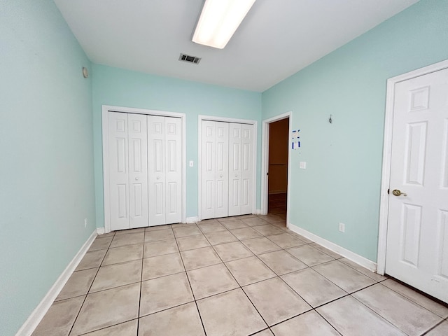 unfurnished bedroom featuring light tile patterned floors and two closets