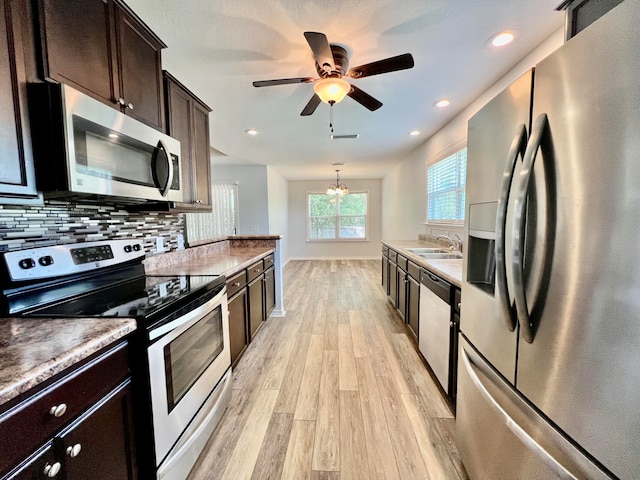 kitchen featuring ceiling fan with notable chandelier, light hardwood / wood-style flooring, stainless steel appliances, sink, and decorative backsplash