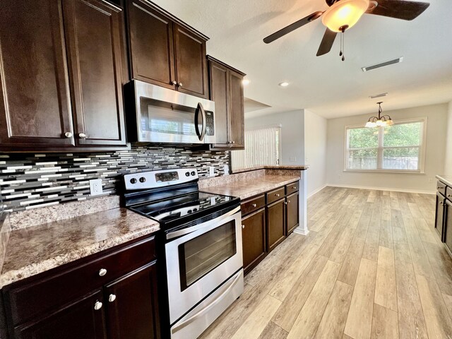 kitchen with decorative light fixtures, ceiling fan with notable chandelier, appliances with stainless steel finishes, light hardwood / wood-style floors, and tasteful backsplash