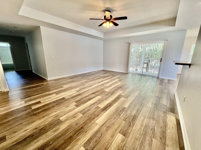 unfurnished living room featuring ceiling fan, wood-type flooring, and a tray ceiling