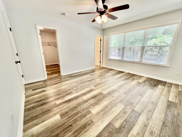 unfurnished bedroom with ceiling fan, a walk in closet, light wood-type flooring, and a closet