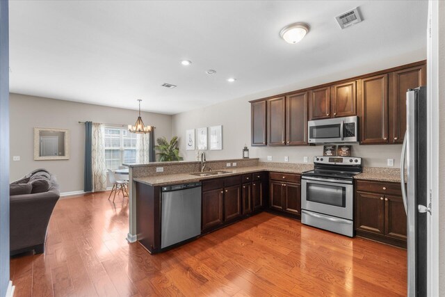 kitchen with an inviting chandelier, light wood-type flooring, appliances with stainless steel finishes, light stone counters, and kitchen peninsula