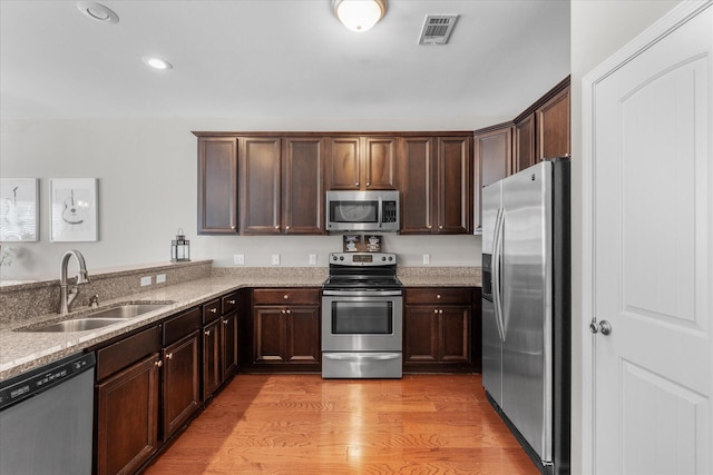 kitchen featuring appliances with stainless steel finishes, light hardwood / wood-style flooring, sink, and light stone counters