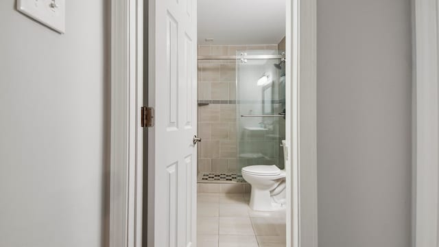 bathroom featuring toilet, a shower with door, and tile patterned floors