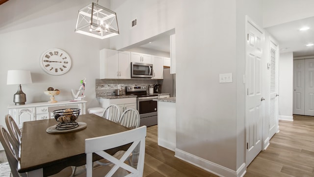 dining room featuring a towering ceiling, light hardwood / wood-style flooring, and a chandelier