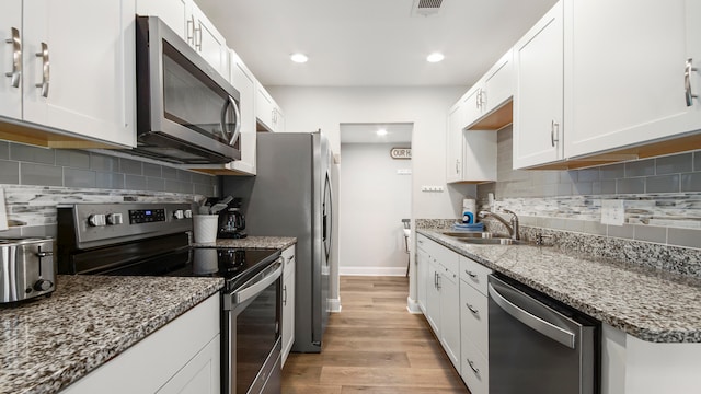 kitchen featuring sink, light wood-type flooring, decorative backsplash, stainless steel appliances, and white cabinets