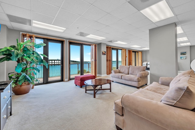 living room with carpet, a water view, and a drop ceiling