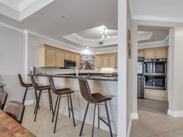 kitchen with a tray ceiling, appliances with stainless steel finishes, light brown cabinets, and a kitchen breakfast bar