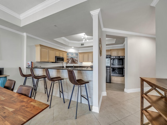 kitchen with a tray ceiling, stainless steel microwave, light tile patterned flooring, and a breakfast bar area