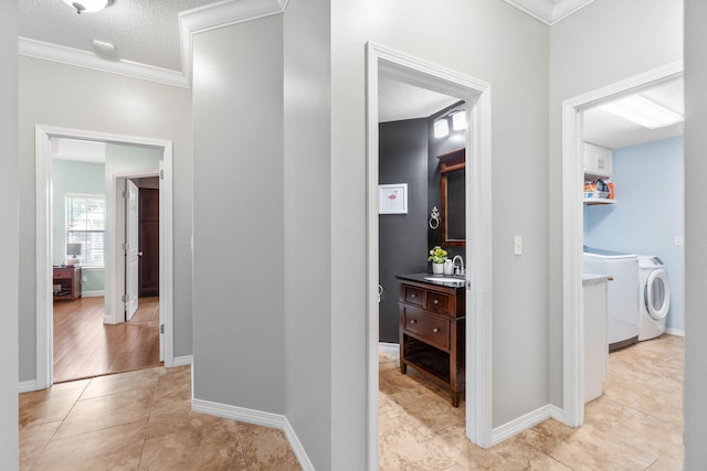 hall with ornamental molding, light tile patterned floors, washer and clothes dryer, sink, and a textured ceiling