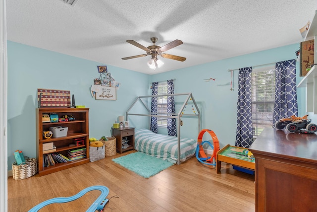 bedroom with a textured ceiling, ceiling fan, and light hardwood / wood-style floors