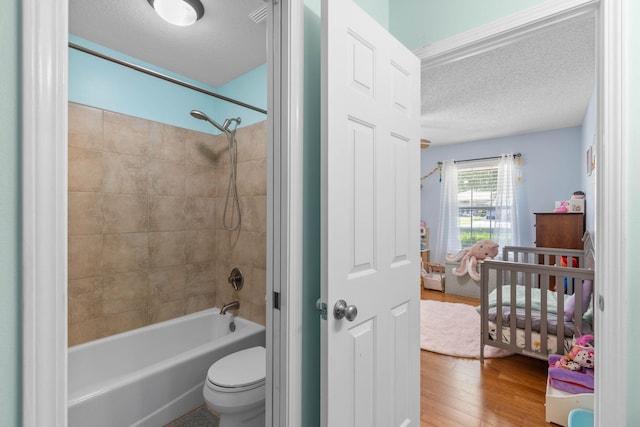 bathroom with a textured ceiling, toilet, tiled shower / bath combo, and hardwood / wood-style flooring