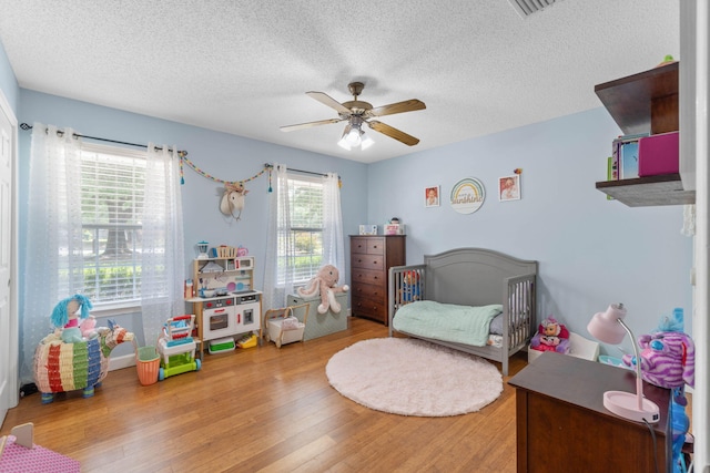 bedroom featuring multiple windows, a nursery area, hardwood / wood-style floors, and ceiling fan