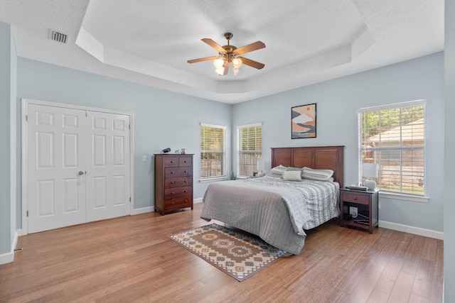 bedroom featuring light hardwood / wood-style floors, ceiling fan, and a tray ceiling