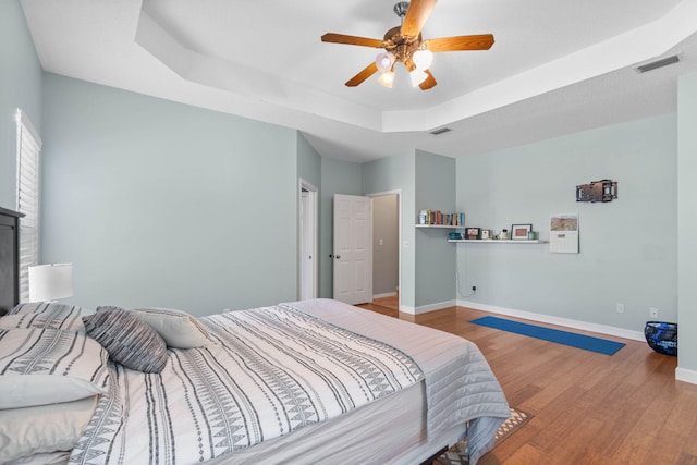 bedroom with ceiling fan, a raised ceiling, and hardwood / wood-style flooring