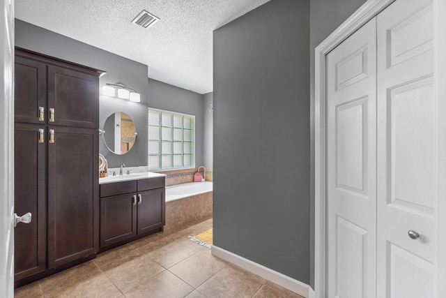 bathroom with tile patterned floors, a textured ceiling, tiled tub, and vanity