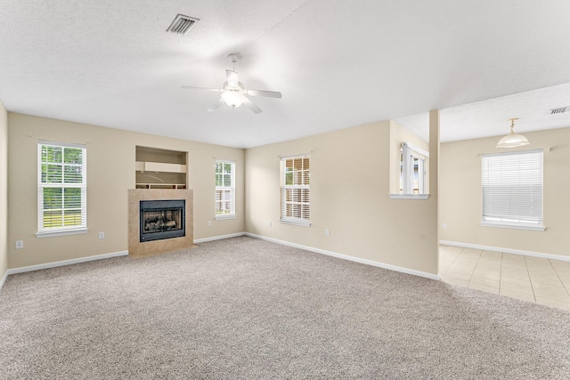 unfurnished living room featuring light carpet, a tiled fireplace, and plenty of natural light