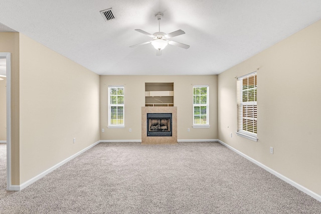 unfurnished living room featuring a tile fireplace, a healthy amount of sunlight, light carpet, and ceiling fan